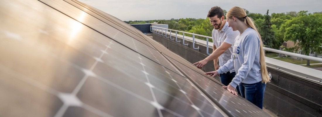 Two students on the roof looking at solar panels.